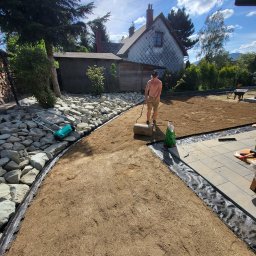 Hermes GardenBud - Mężczyzna wałuje ziemię w ogrodzie, przygotowując teren pod trawnik. Widoczne kamienie, trawa, dom w tle i narzędzia ogrodnicze.