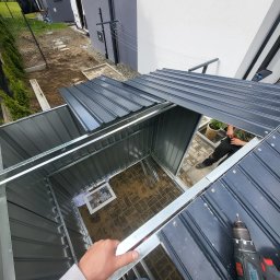 Hermes GardenBud - Montaż metalowego domku narzędziowego w ogrodzie, widok z góry na częściowo zadaszoną konstrukcję. W tle budynek mieszkalny i fragment ogrodu.