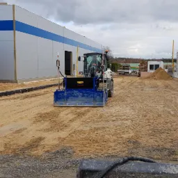 Niwelacja terenu pod budowę hali przemysłowej za pomocą miniładowarki z osprzętem do rozprowadzania i wyrównywania podłoża.