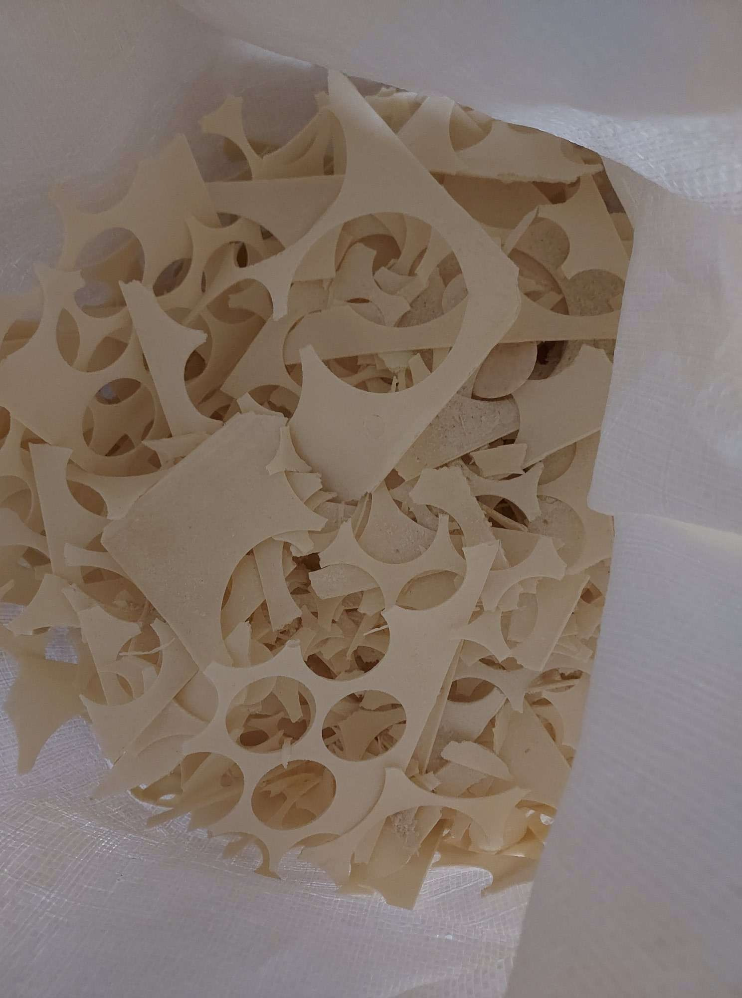 Suszone płatki zbożowe o nieregularnych kształtach z okrągłymi otworami wewnątrz, widoczne w białym worku z tworzywa sztucznego.