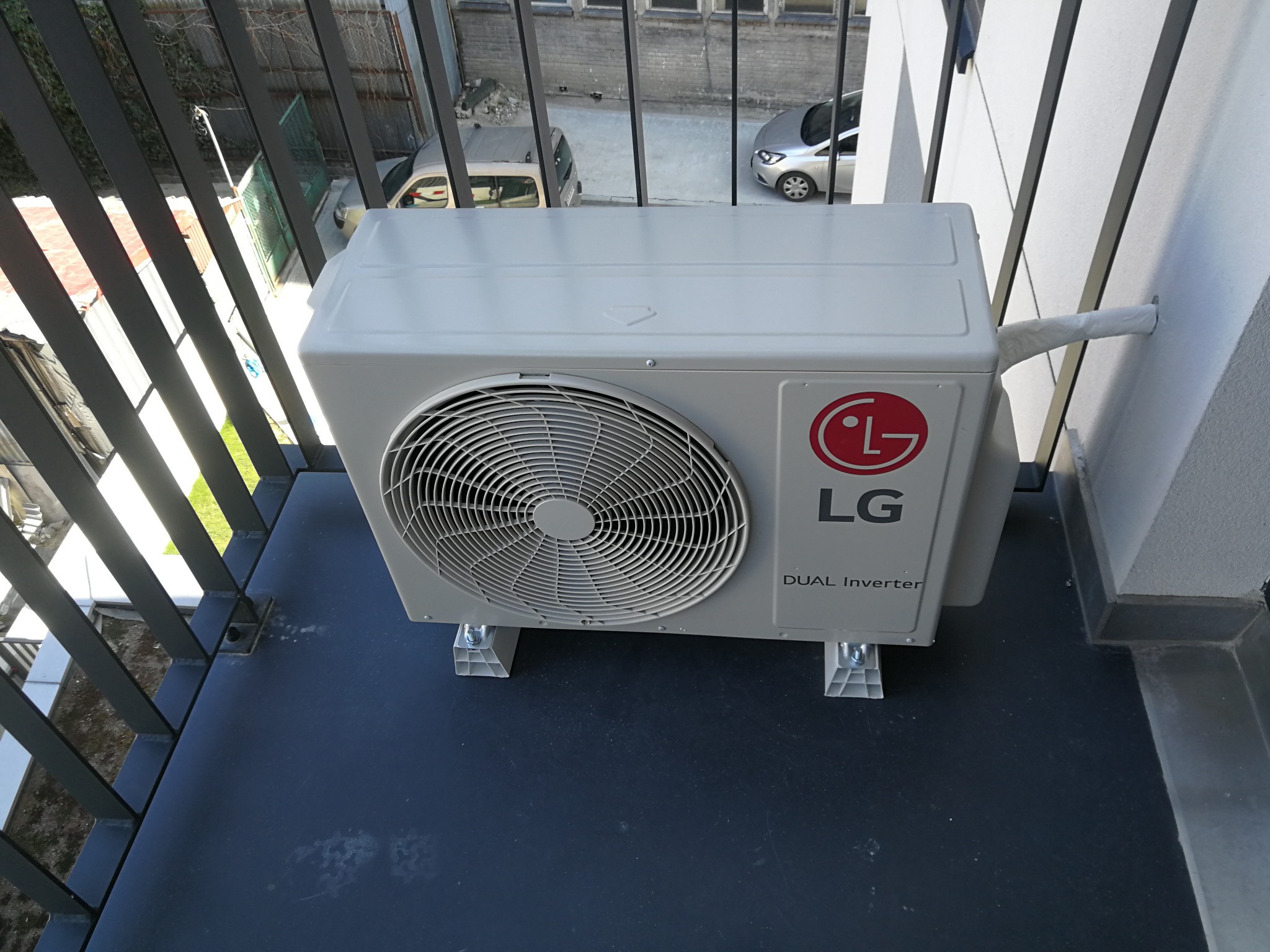 Zewnętrzna jednostka klimatyzacji LG Dual Inverter zamontowana na balkonie, widoczne mocowania i rura odprowadzająca skropliny zabezpieczona folią.