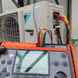 Pomiar parametrów elektrycznych klimatyzatora Daikin R32 Inverter za pomocą pomarańczowego miernika z kolorowymi przewodami pomiarowymi.