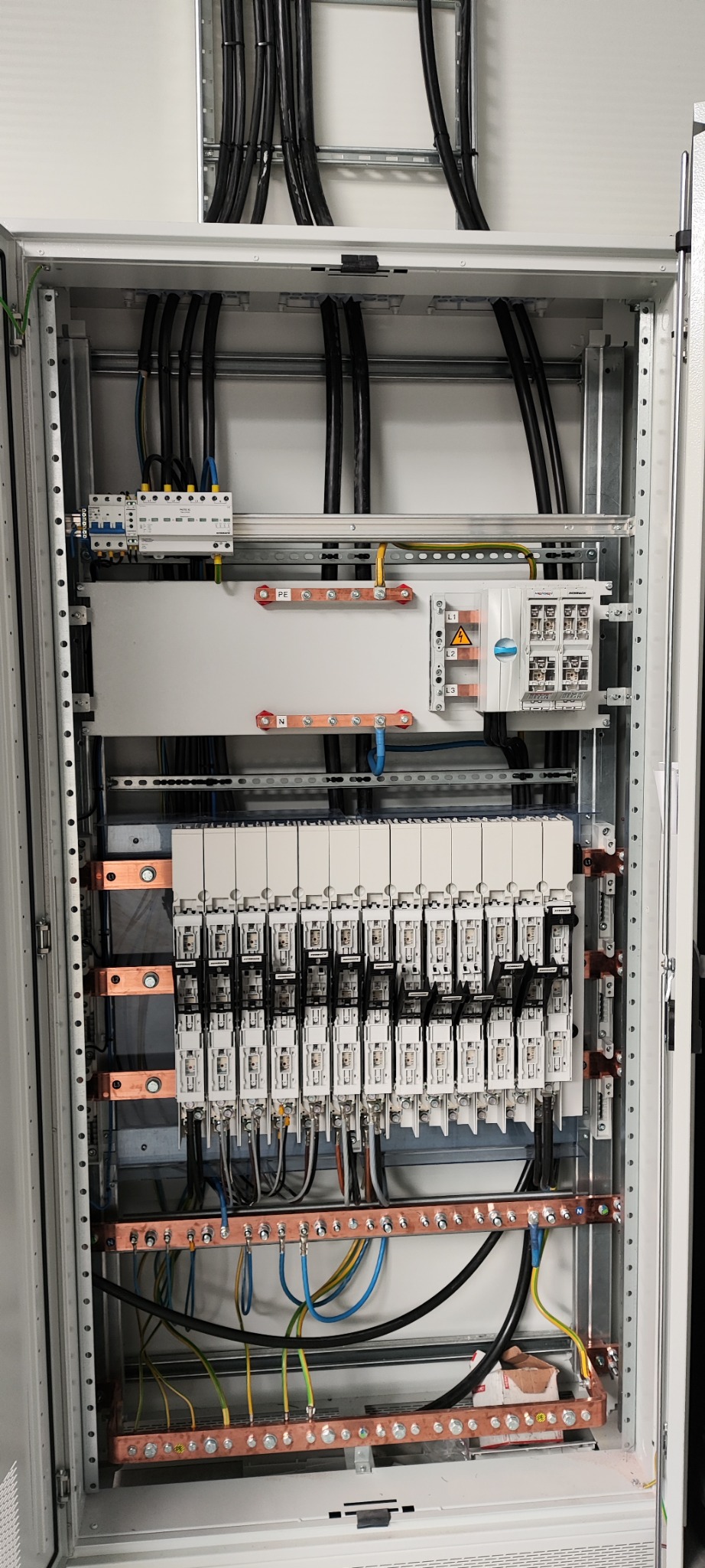 Wnętrze rozdzielnicy elektrycznej z widocznymi przewodami, listwami zaciskowymi i zabezpieczeniami, uporządkowane okablowanie w szafie sterowniczej.