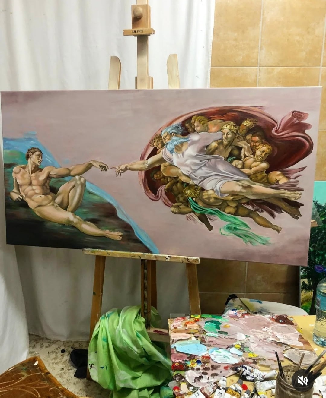 Reprodukcja fresku Michała Anioła 'Stworzenie Adama' na płótnie, ustawiona na drewnianej sztaludze w pracowni artystycznej, widoczna paleta malarska i tubki farb.