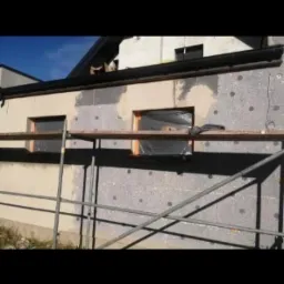 Ocieplanie elewacji styropianem z widocznymi kołkami mocującymi, zabezpieczone okna folią, Karczew.