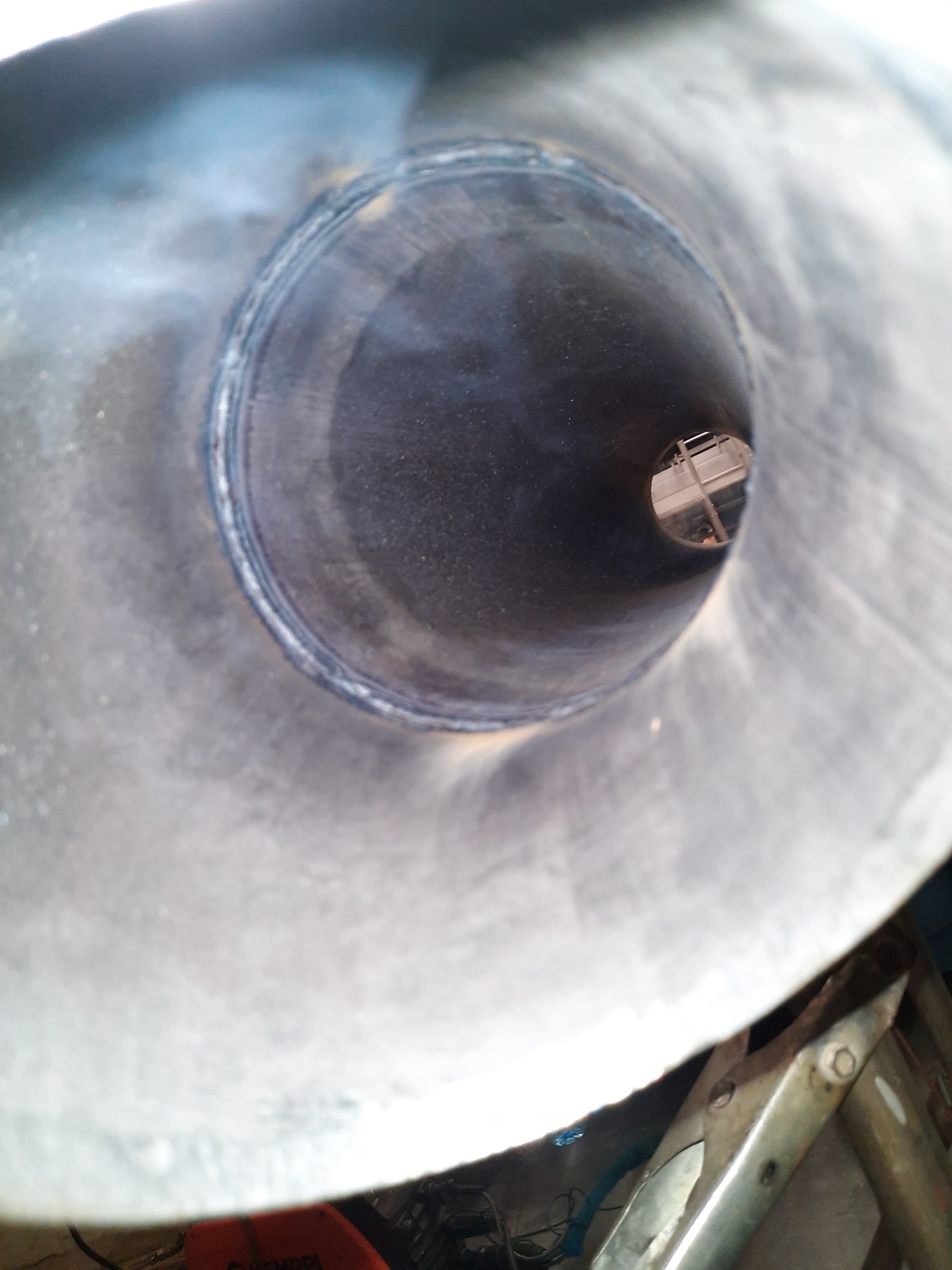 Wnętrze metalowej rury z widocznym spoiną, sfotografowane pod kątem z perspektywy wnętrza rury, w tle widoczny fragment drabiny.