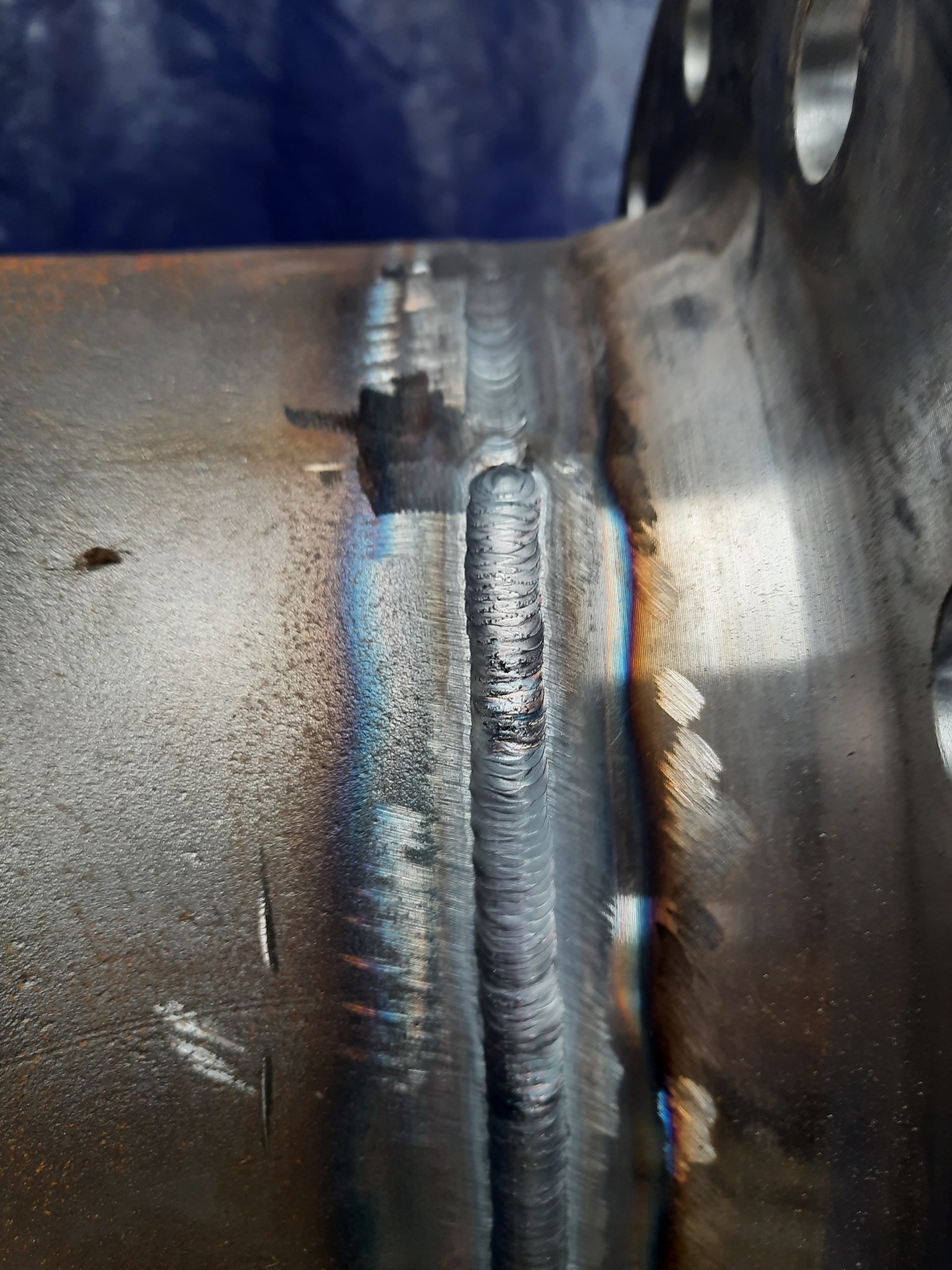 Spoina na metalowej rurze z widocznymi śladami ciepła i przebarwieniami, złącze kołnierzowe w tle.