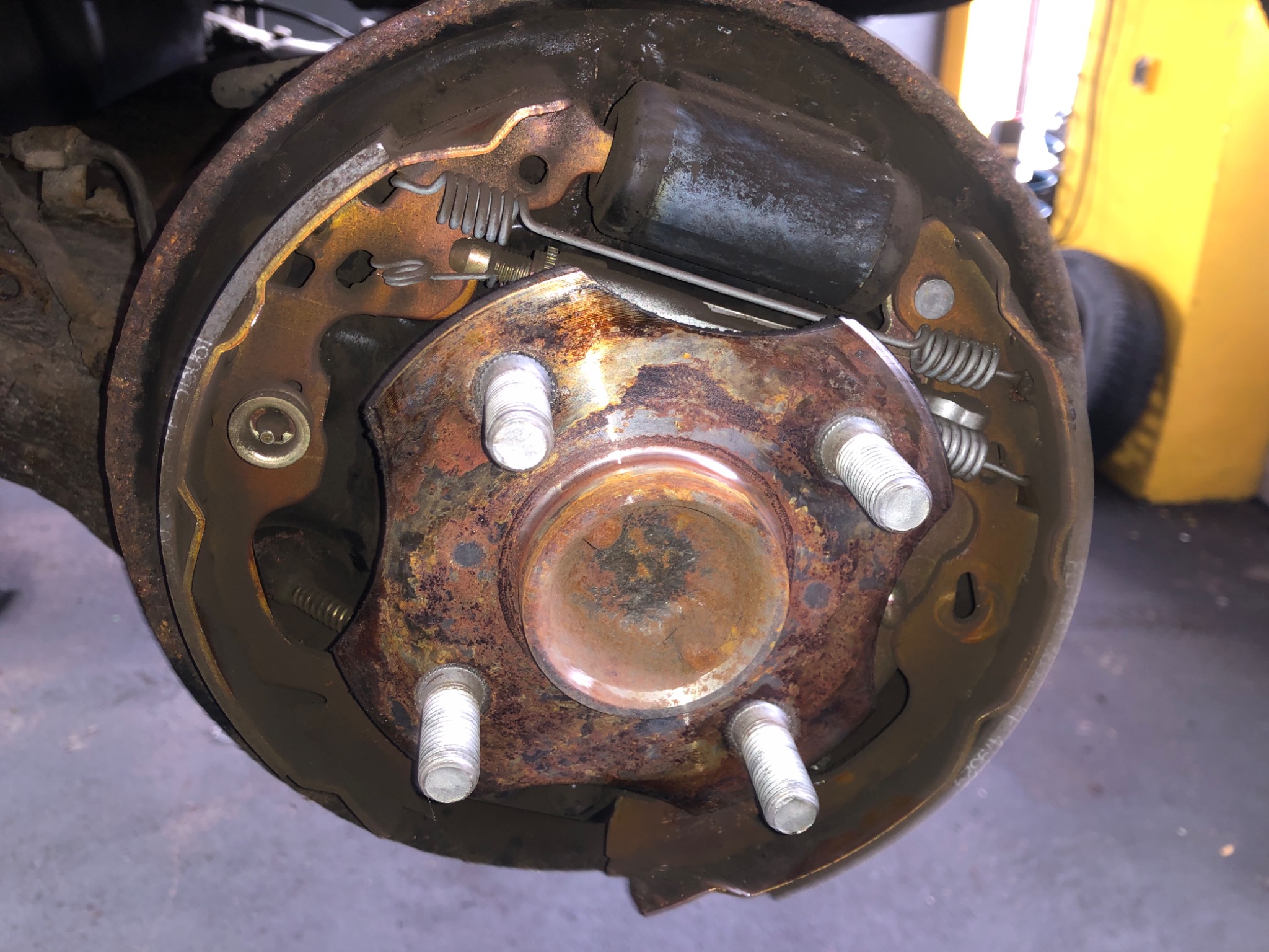 Otwarty bęben hamulcowy z widocznymi szczękami, sprężynami i cylindrem, silna korozja na elementach metalowych.