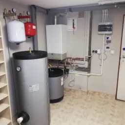 Instalacja grzewcza w piwnicy w Poznaniu: Dwa zbiorniki akumulacyjne Ferroli, biały i czerwony zbiornik przeponowy, oraz biały piec centralnego ogrzewania z widoczną instalacją hydrauliczną.