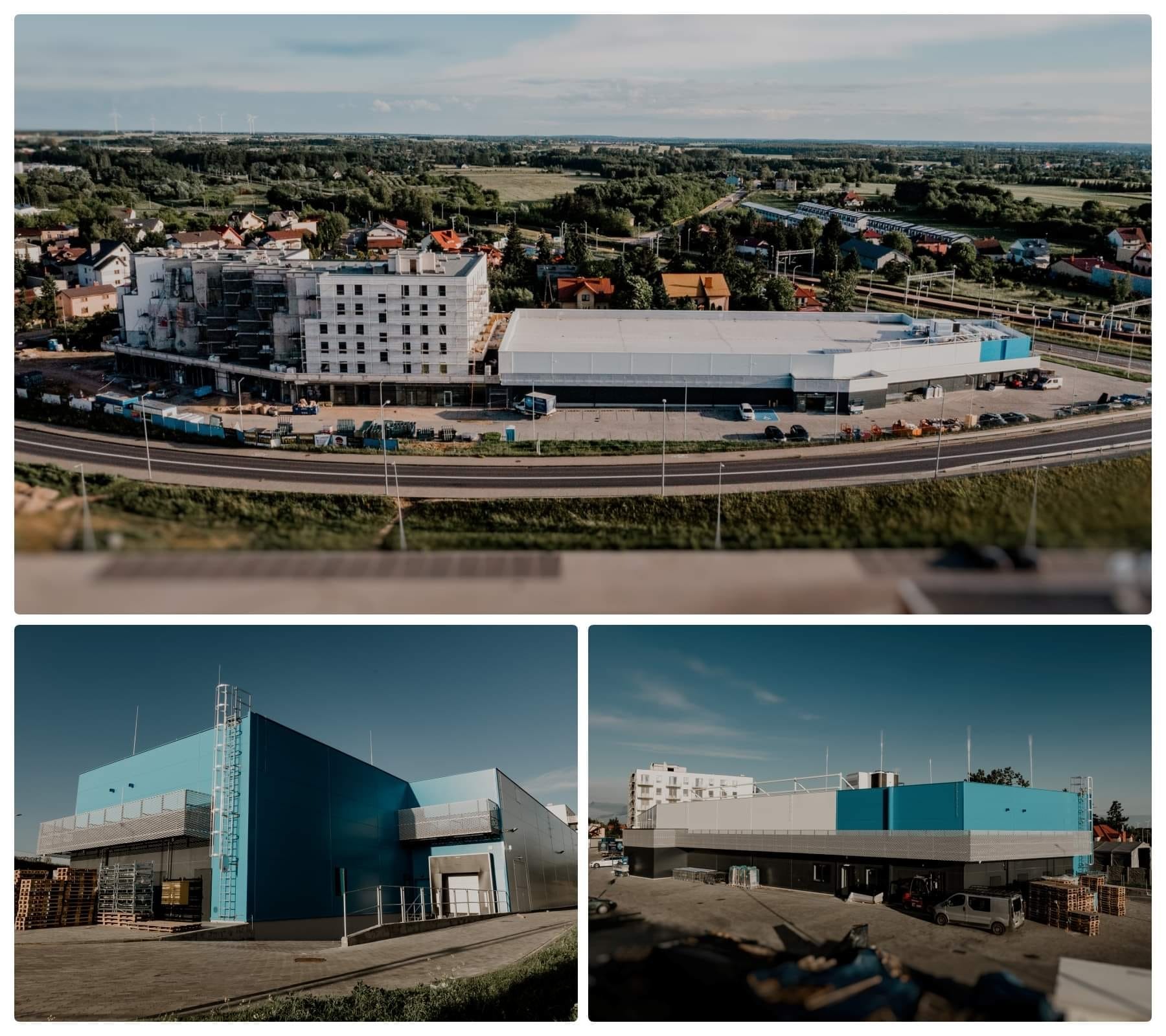 Widok z góry na budynek w trakcie budowy, z widocznymi rusztowaniami i nowo wybudowaną halą magazynową z niebieskimi elementami elewacji.