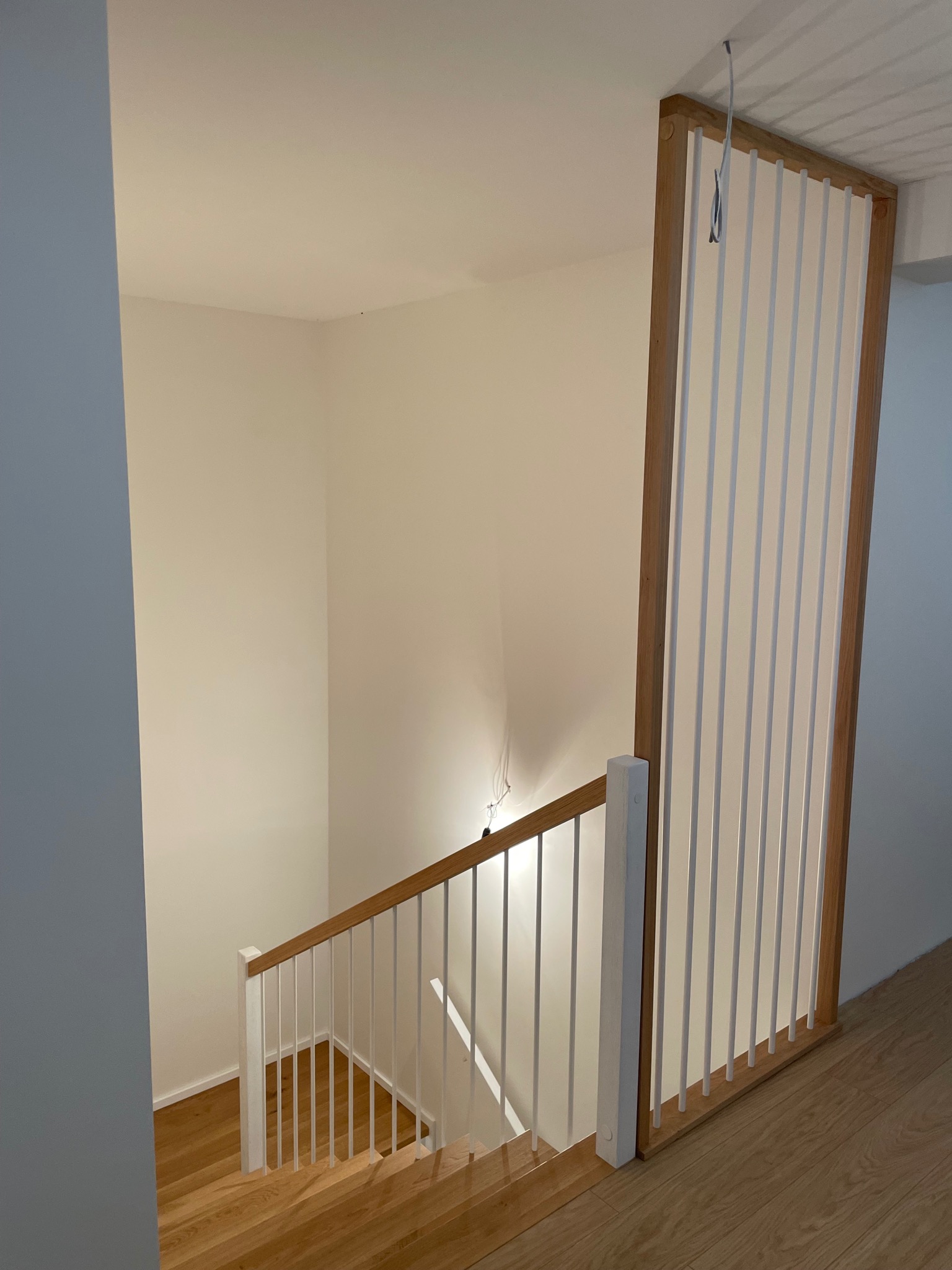 Jasne, drewniane schody z białą balustradą w nowoczesnym wnętrzu. Ujęcie z góry, widoczne detale wykończenia i oświetlenie.