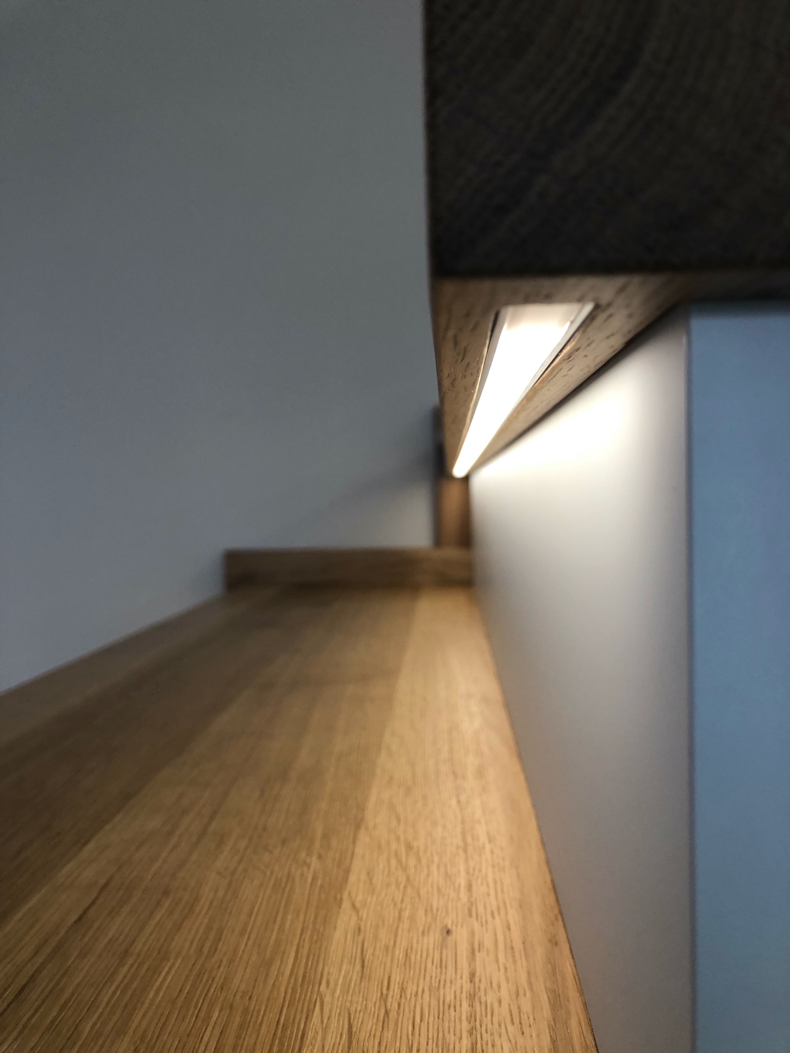 Detal drewnianego blatu z oświetleniem LED, widok z dołu, ukazujący strukturę drewna i subtelne światło, minimalistyczny design.