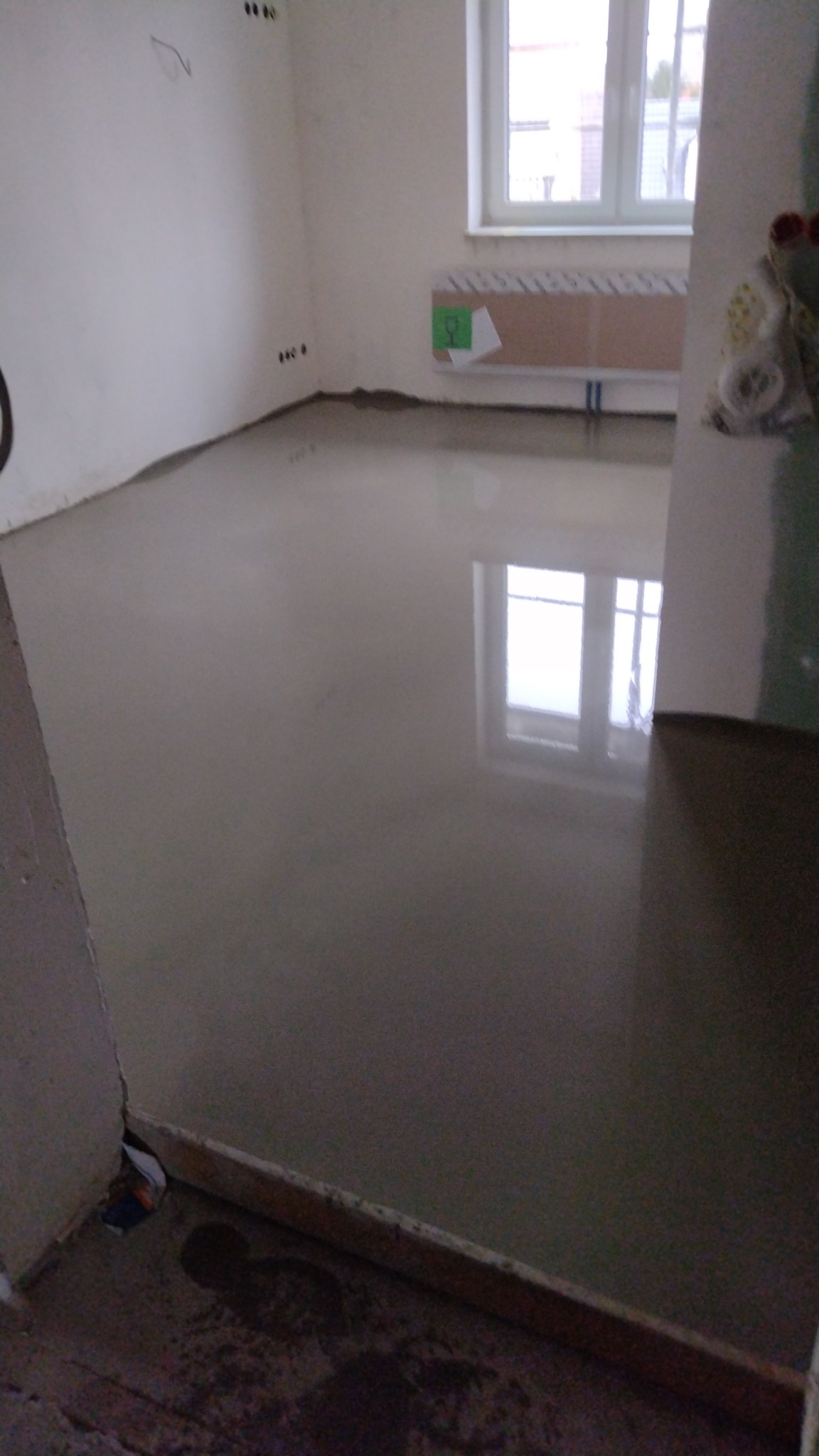 Świeżo wylana, mokra wylewka samopoziomująca w pokoju z oknem, widoczne ślady po wylewce na ścianach.
