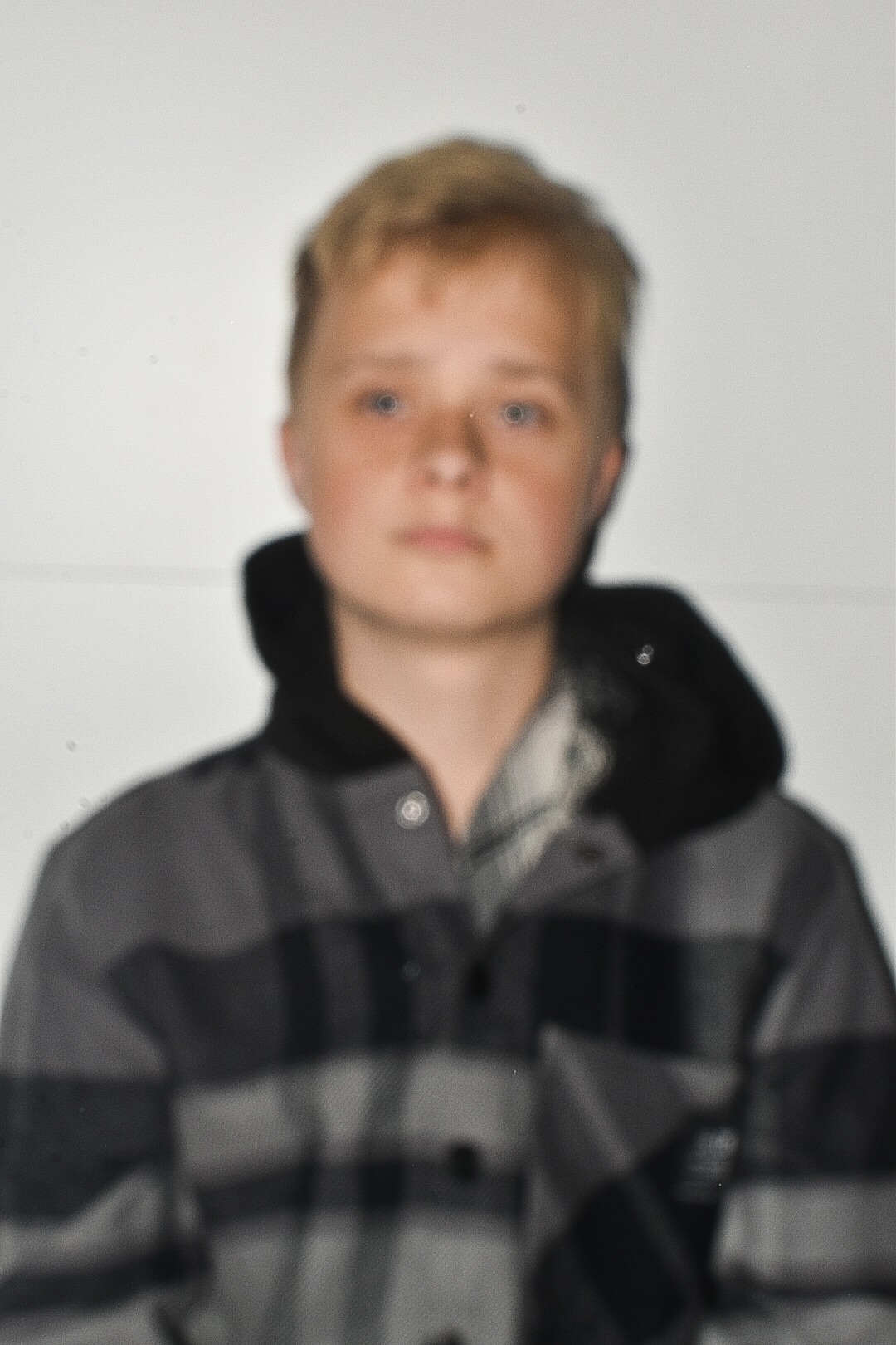Portret nastolatka z blond włosami i niebieskimi oczami w szarej koszuli w kratę z kapturem na białym tle, lekko rozmazany obraz.