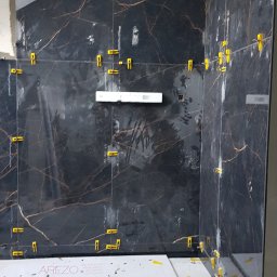 Róża Kołtun - Montaż płytek imitujących marmur w łazience, widoczne poziomica, młotek i żółte krzyżyki dystansowe.