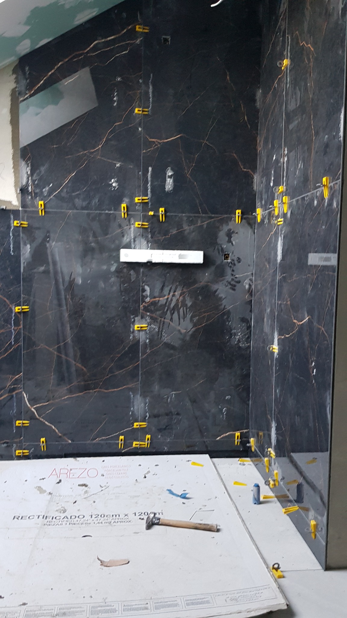 Montaż płytek imitujących marmur w łazience, widoczne poziomica, młotek i żółte krzyżyki dystansowe.