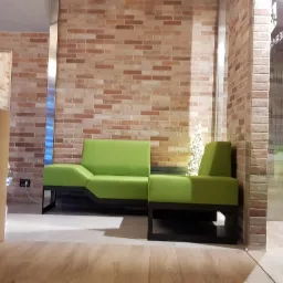 Wnętrze biura z ceglaną ścianą, zielonymi sofami modułowymi na czarnych nogach, roślinami doniczkowymi i choinką ze światełkami.