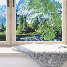 Okno PCV z widokiem na górski krajobraz, parapet zdobi miękki, biało-szary pled.