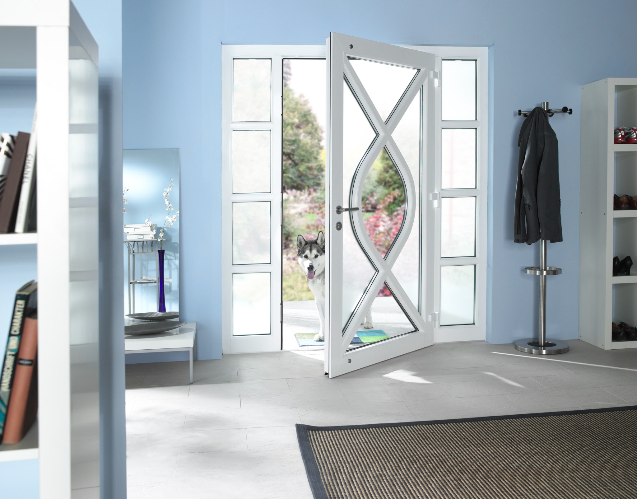Nowoczesne drzwi balkonowe z białymi ramami i dekoracyjnym szprosowaniem, przez które widać psa rasy husky w ogrodzie, jasne wnętrze z niebieskimi ścianami.