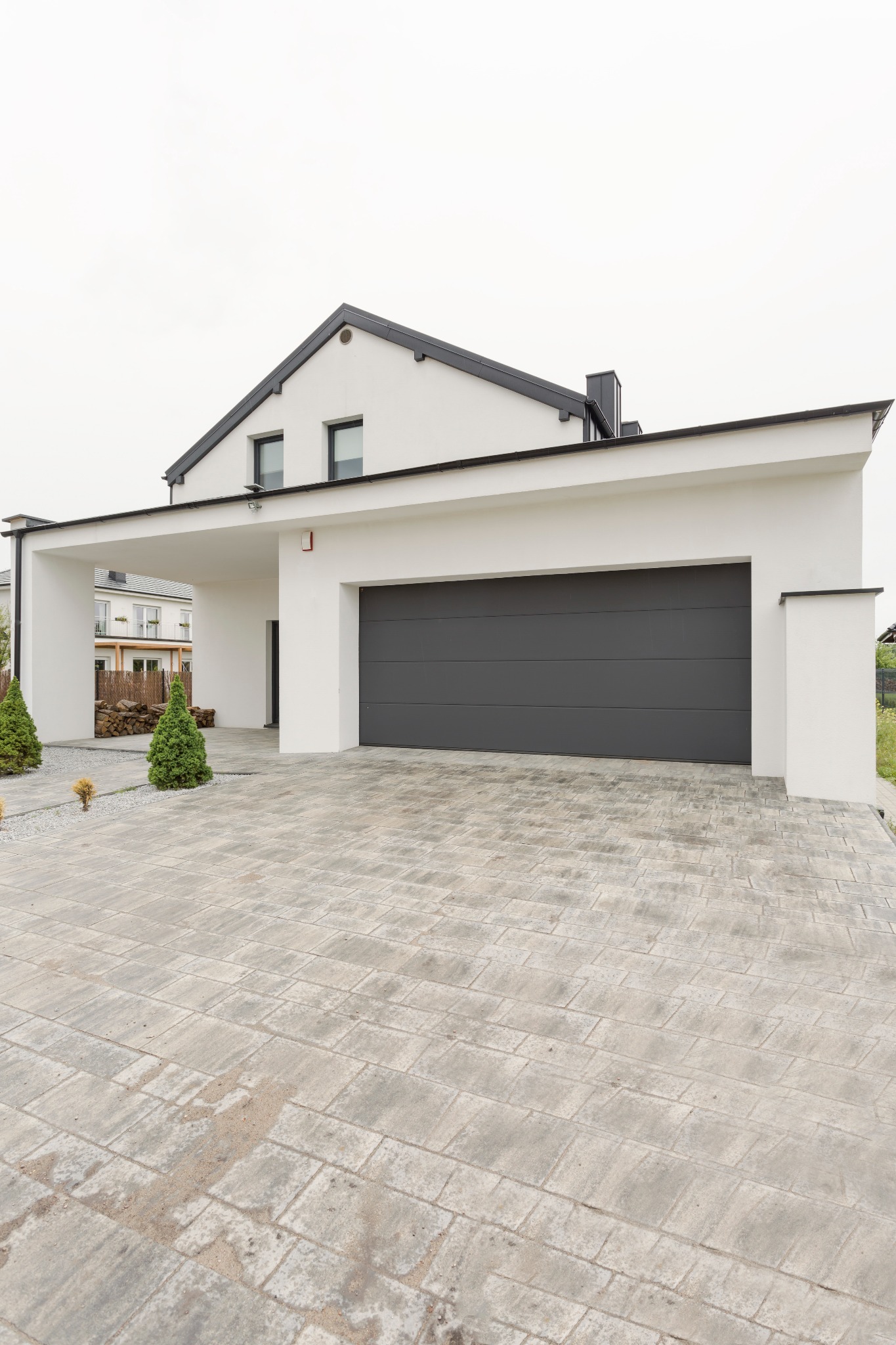 Nowoczesny dom z garażem i szarą bramą segmentową, widok z zewnątrz na podjazd wyłożony kostką brukową.