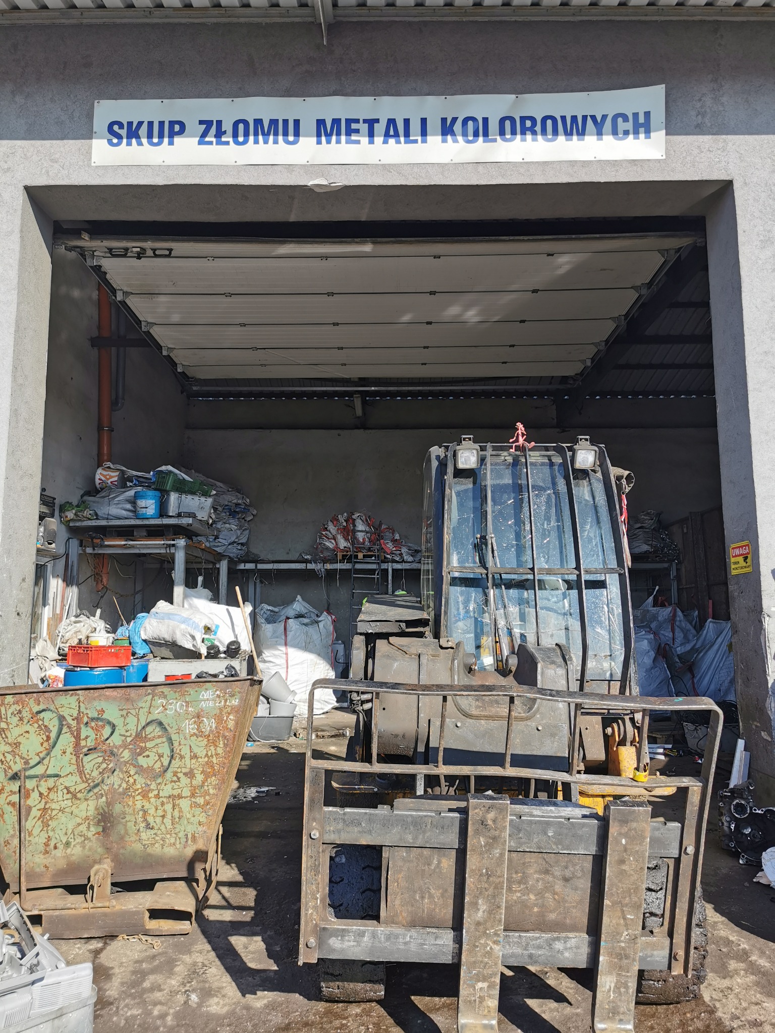 Wnętrze punktu skupu złomu metali kolorowych z widocznym wózkiem widłowym i kontenerem na odpady.