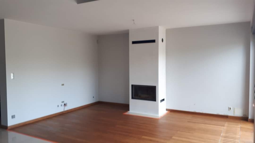 Wnętrze pokoju po malowaniu ścian na szaro, z drewnianą podłogą i nowoczesnym białym kominkiem z czarnym wkładem, widoczne niedokończone wykończenia przy podłodze.