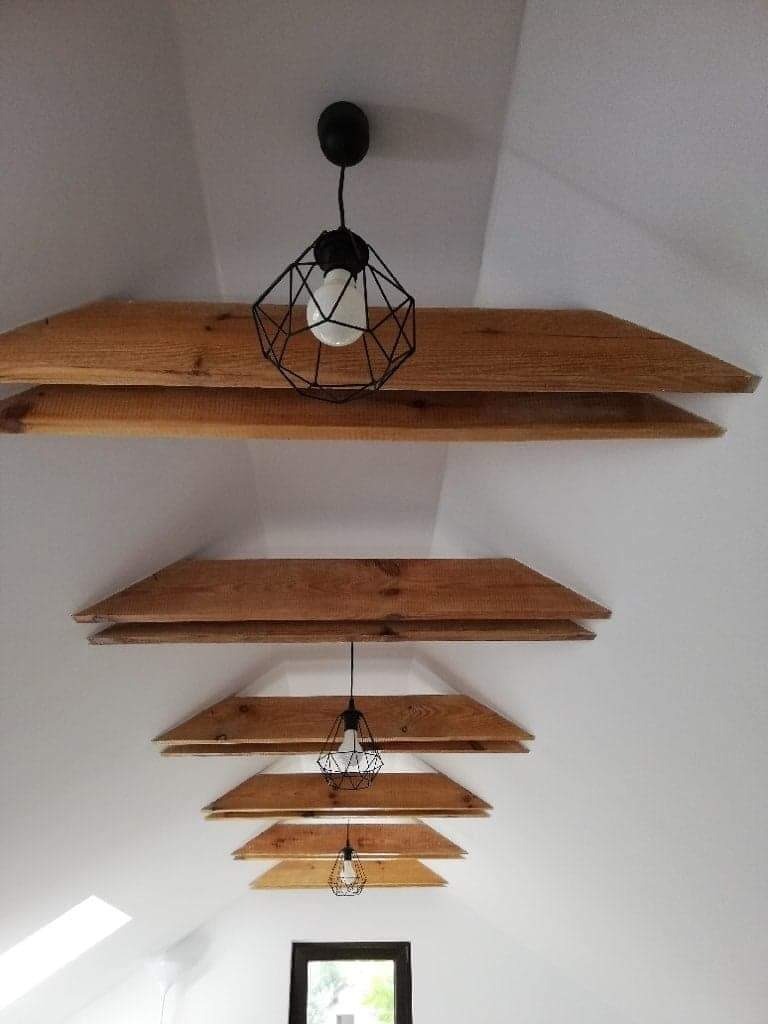 Białe poddasze z drewnianymi belkami stropowymi i trzema czarnymi lampami drucianymi w stylu industrialnym, widok z dołu.