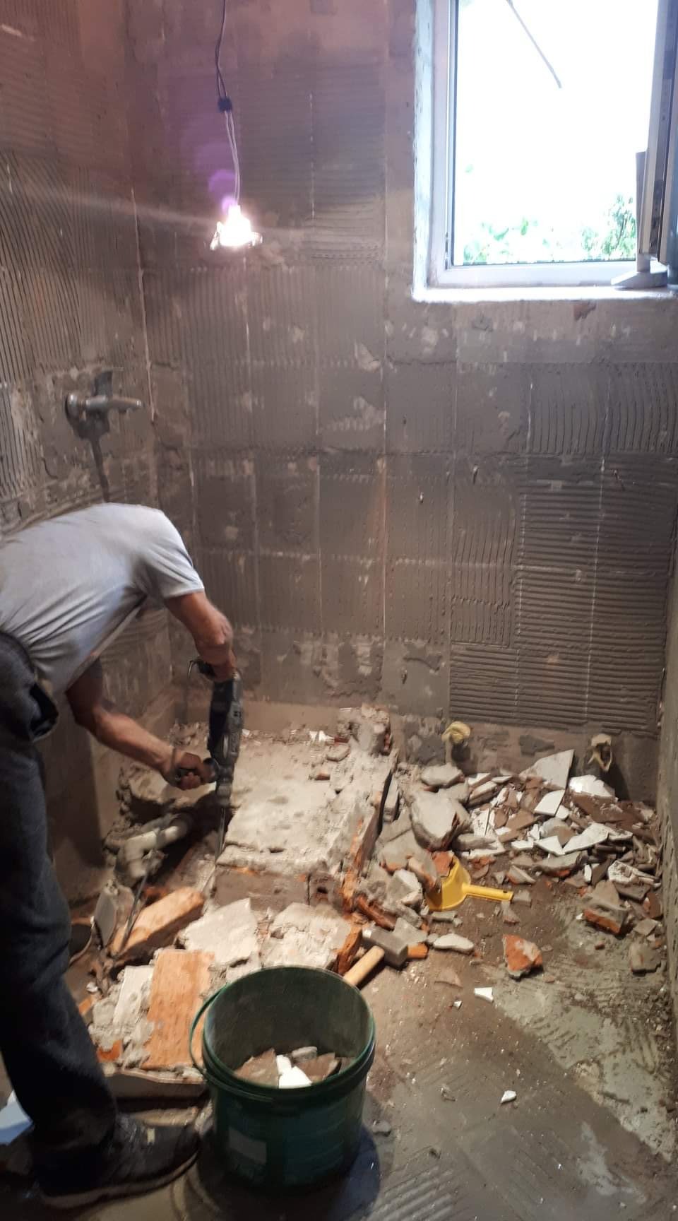 Demontaż płytek w łazience we Wrześni przy użyciu młota udarowego, widoczne gruz i przygotowane ściany pod nowe płytki, kubeł na odpady.