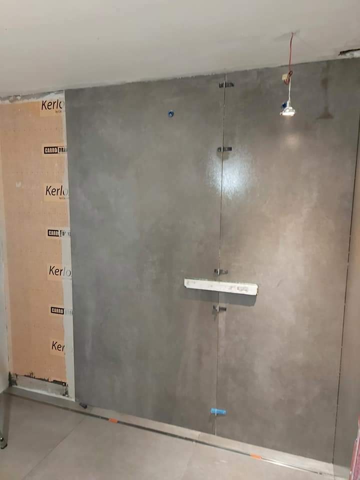 Montaż wielkoformatowych płyt ściennych w łazience, widoczne płyty Kerlo i listwa poziomująca, surowa aranżacja, punktowe oświetlenie.