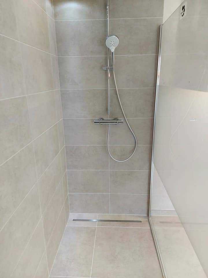 Kabina prysznicowa walk-in z odpływem liniowym, wykończona beżowymi płytkami w poziomym układzie.