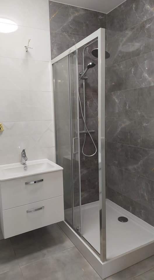 Nowoczesna łazienka z kabiną prysznicową z przesuwnymi drzwiami, umywalką nablatową z szafką i szarymi płytkami imitującymi marmur na ścianie.