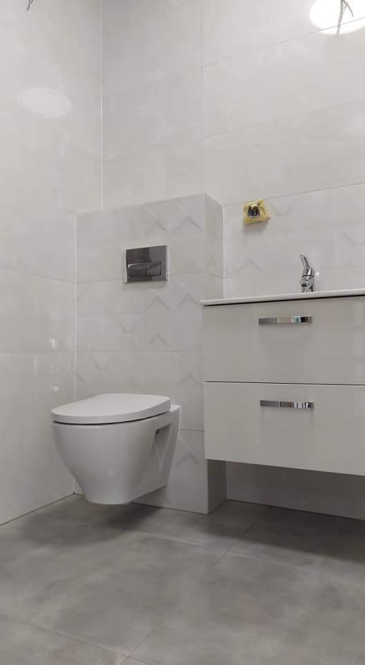 Nowoczesna łazienka w bieli i szarości, z podwieszaną toaletą, umywalką z szafką i płytkami z subtelnym wzorem 3D na ścianie.