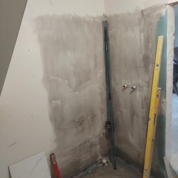 Top Glazur - Przygotowanie ścian pod płytki w narożniku łazienki, widoczne piony wodne, poziomice i płytka podłogowa.