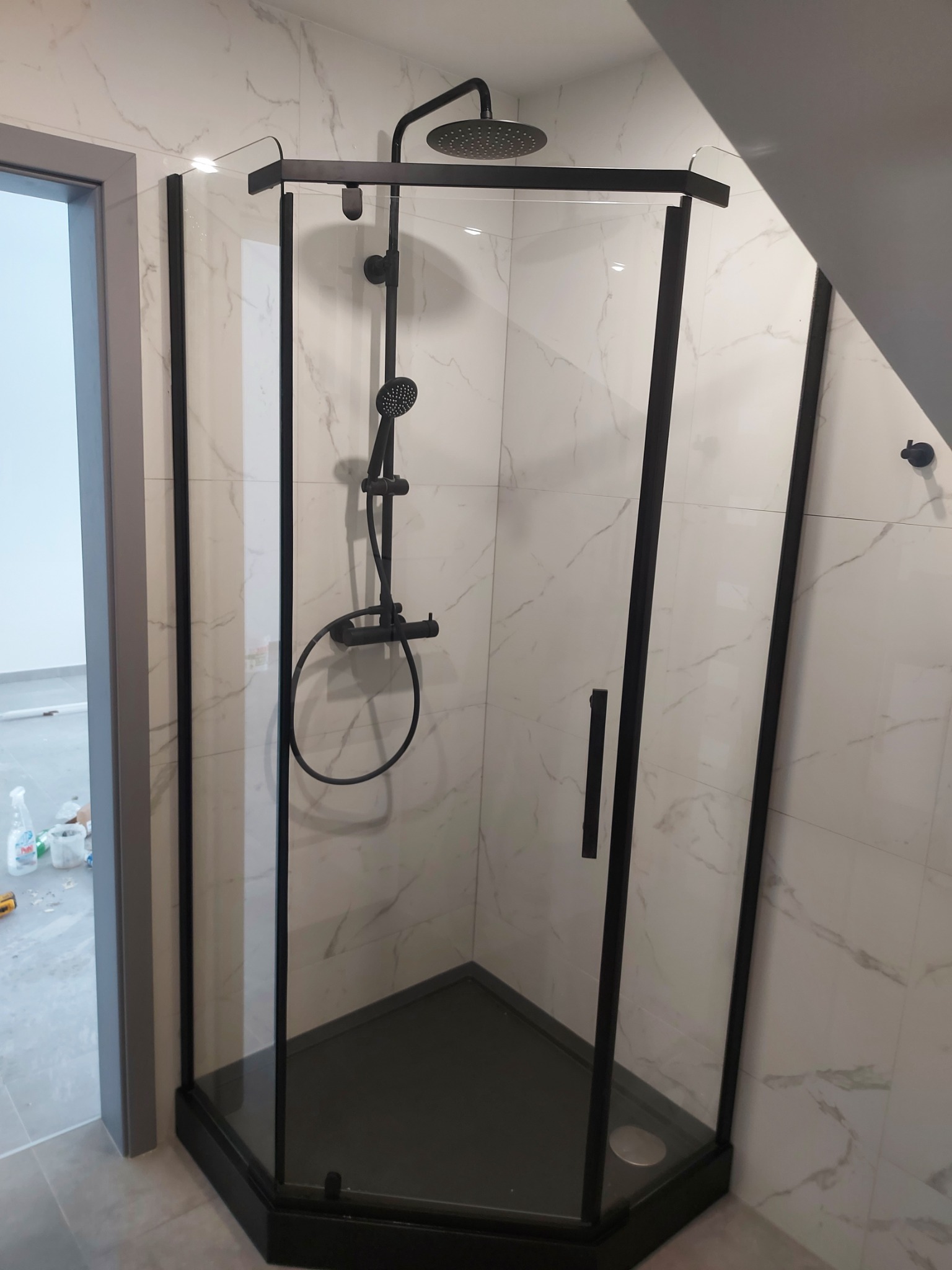 Nowoczesna kabina prysznicowa z czarnymi profilami i deszczownicą, marmurowe płytki na ścianach, ukośny sufit.