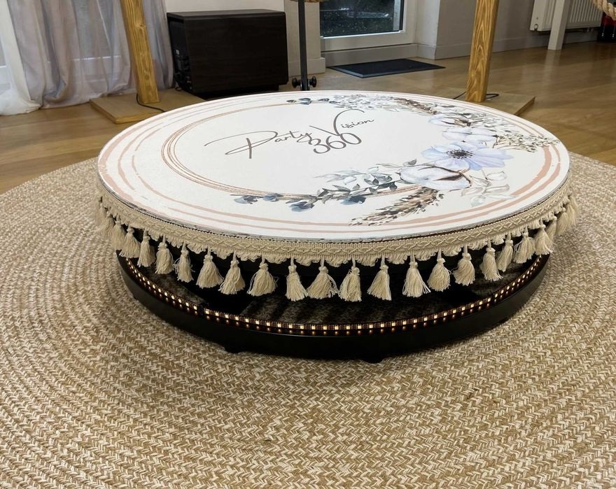 Okrągła platforma obrotowa z dekoracyjnym nadrukiem kwiatowym i frędzlami, podświetlona diodami LED, umieszczona na okrągłym dywanie.