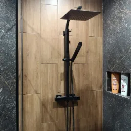 Nowoczesna kabina prysznicowa z czarną armaturą, drewnopodobne płytki na ścianie i wnęka z kosmetykami, aranżacja łazienki.