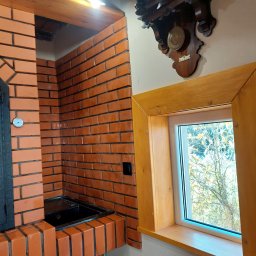 PEKASA Serhii Lypianchyk - Murowany kominek z czerwonej cegły, z czarnym wkładem i termometrem, obok okno w drewnianej ramie i stary zegar na ścianie. Widok z dołu.