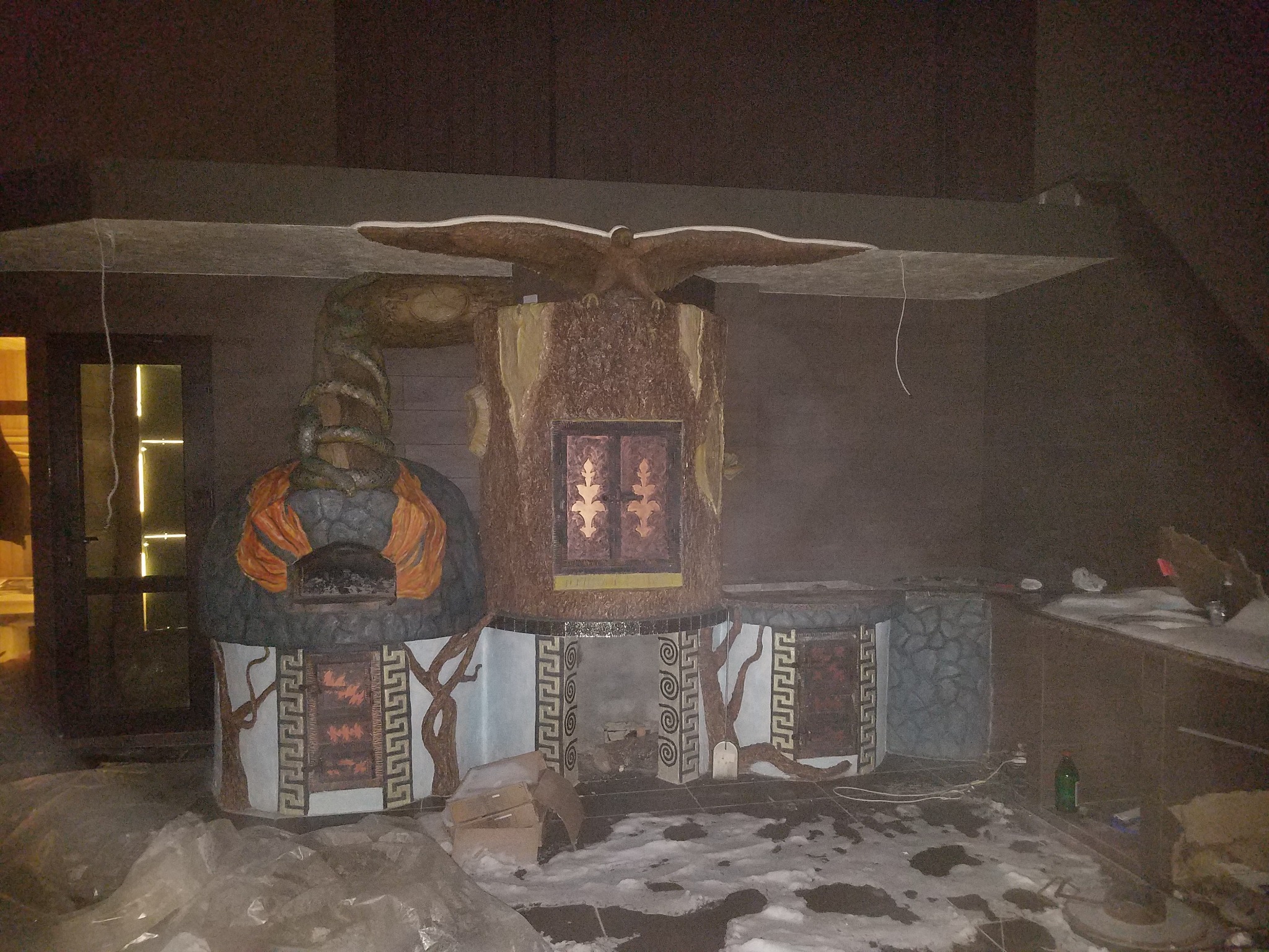 Unikatowy piec chlebowy z motywem orła i drzew, zdobiony wzorami greckimi, w pomieszczeniu z elementami wykończenia. Widoczne ślady po budowie.