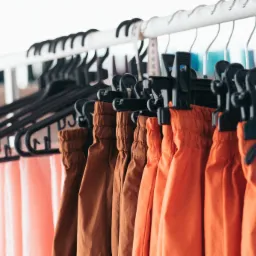 Rząd kolorowych, damskich spodni na wieszakach, z widoczną miarką krawiecką i logo 'MAKO' na jednym z wieszaków.