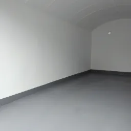 Pomalowane na szaro wnętrze z łukowatym sufitem, widoczne ślady łączeń płyt na suficie i ciemnoszara listwa przypodłogowa.