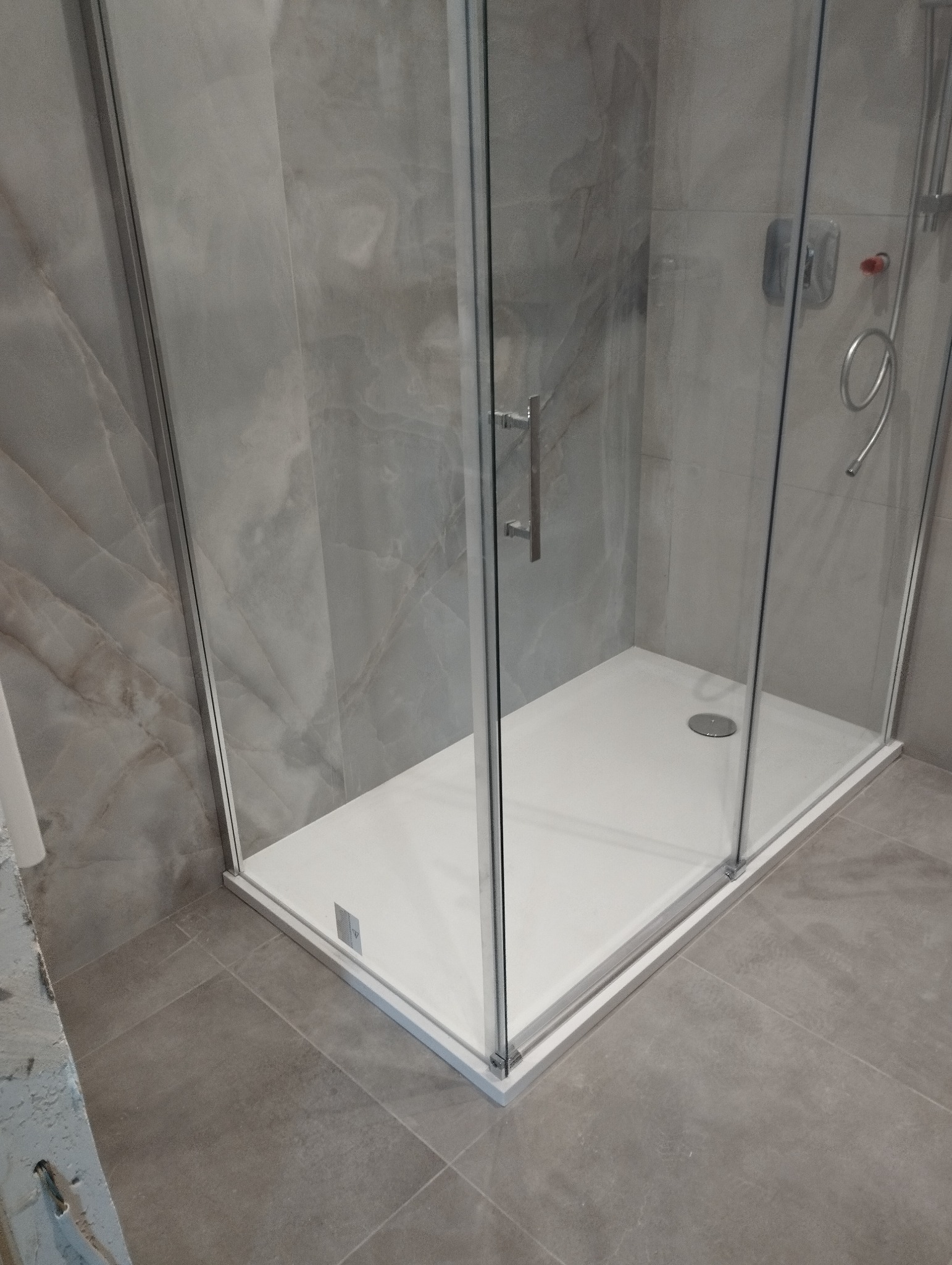 Nowoczesna kabina prysznicowa z białą brodzikiem i szklanymi ścianami na tle płytek imitujących marmur.