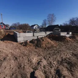 Wznoszenie fundamentów z betonowych bloczków w Gdańsku, widok na plac budowy w słoneczny dzień.