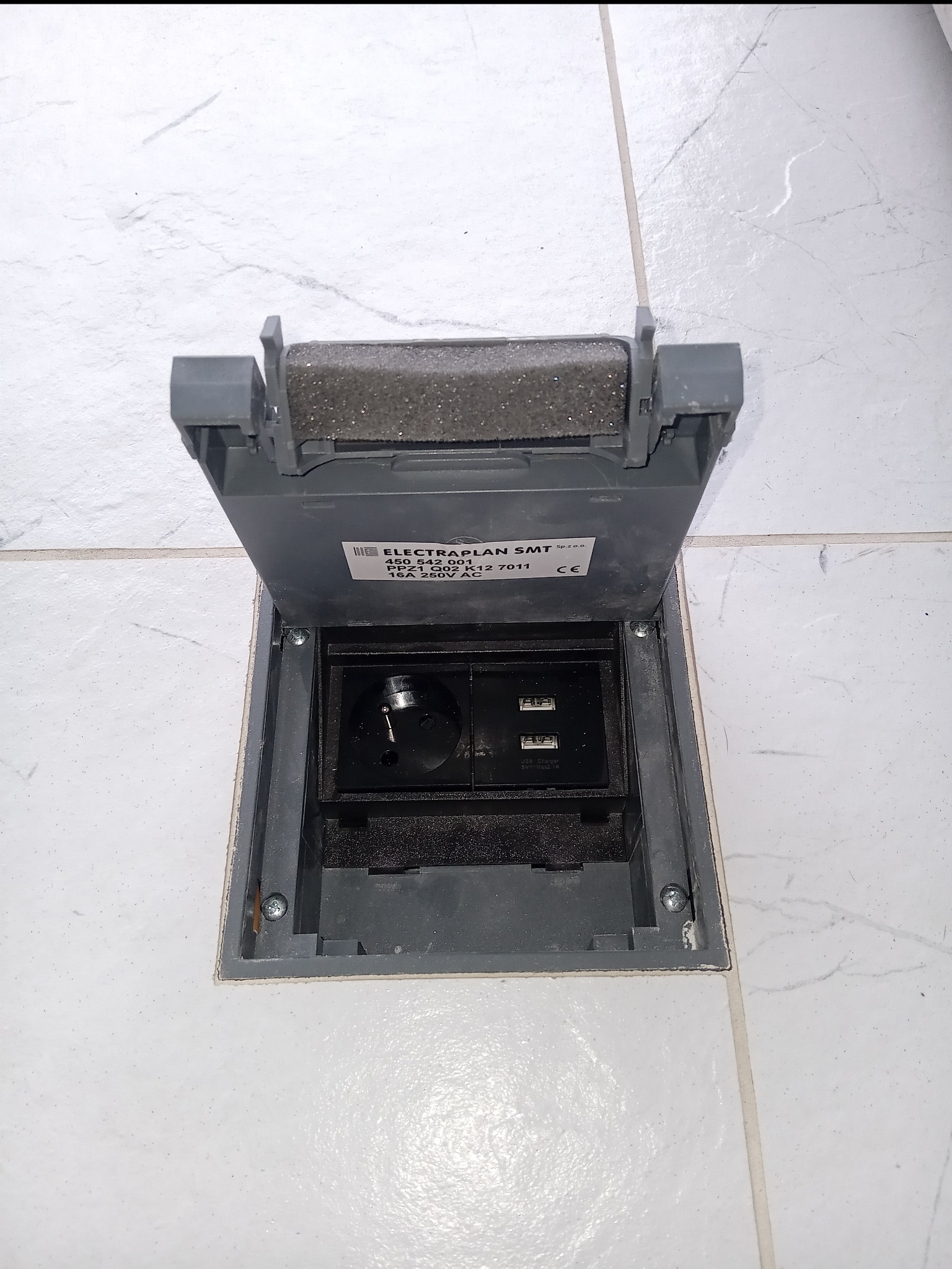 Otwarta podłogowa puszka elektryczna Electraplan SMT z gniazdem zasilającym i dwoma portami USB, wbudowana w jasną, marmurkową podłogę.