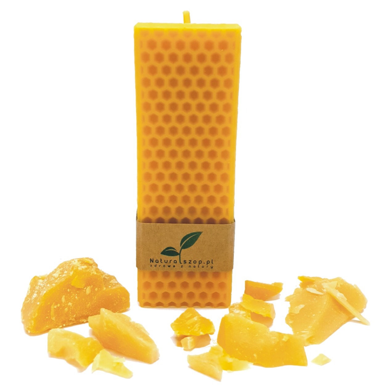 Żółta, prostokątna świeca z wosku pszczelego o strukturze plastra miodu, owinięta brązową etykietą z zielonym listkiem i adresem strony internetowej, otoczona kawałkami surowego wosku pszczelego...