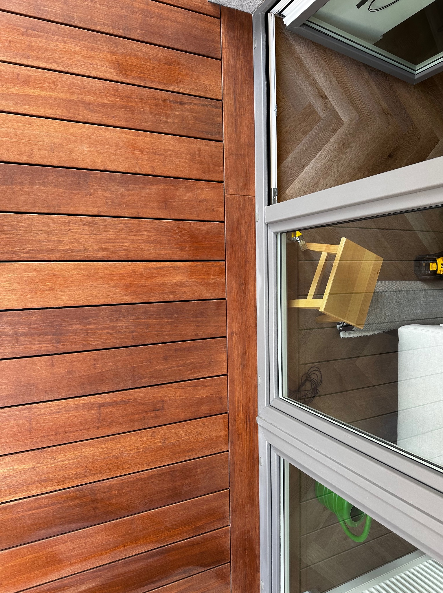 Fragment zabudowy balkonu z desek, widok przez okno na wnętrze. Uwagę przyciąga drewniana okładzina i detale wykończeniowe.