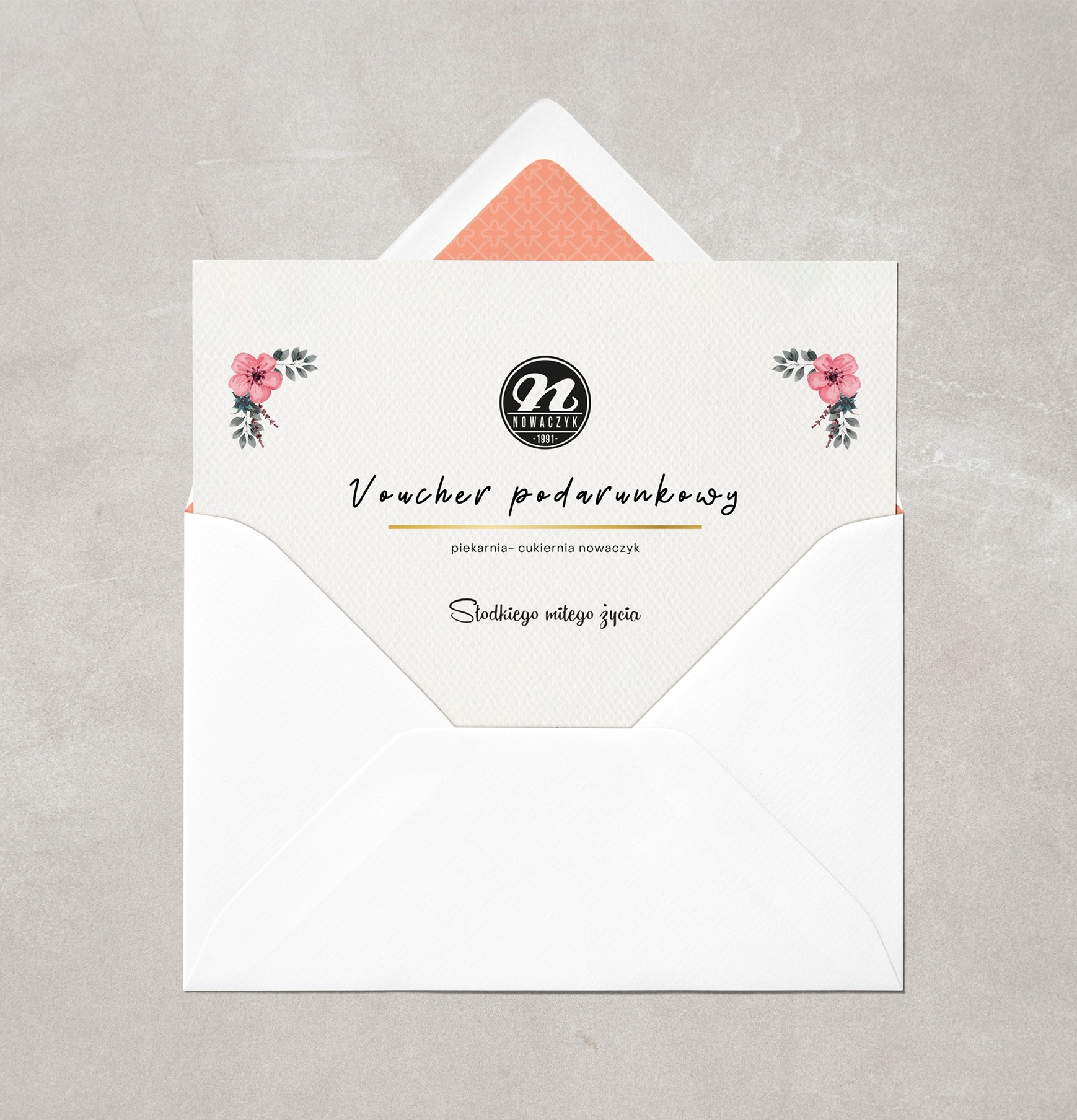Otwarta biała koperta z wyeksponowanym voucherem prezentowym piekarni-cukierni Nowaczyk, zdobionym kwiatowymi motywami i minimalistycznym logo na kremowym tle.