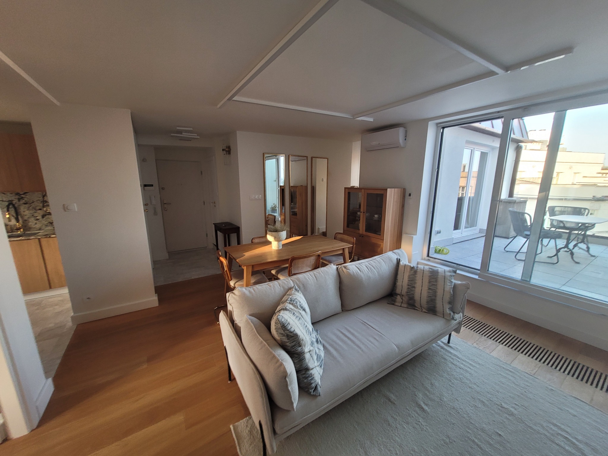 Jasne, przestronne wnętrze mieszkania z widokiem na balkon, drewnianą podłogą i nowoczesnym oświetleniem sufitowym.