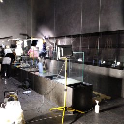 RB-Roman Bratasiuk - Ekipa sprzątająca gabloty w Muzeum Narodowym w Warszawie, widoczny reflektor na żółtym statywie, rolka kabla i butelka ze spryskiwaczem.