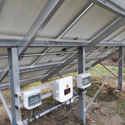 PROMOSOLAR Paweł Gramburg - Montaż paneli słonecznych z widocznym inwerterem i zabezpieczeniami elektrycznymi w Serocku, widok od spodu konstrukcji wsporczej.