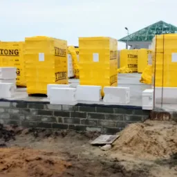 Fundament z cegły i bloczki Ytong w żółtej folii, widoczny szkielet dachu w budowie.